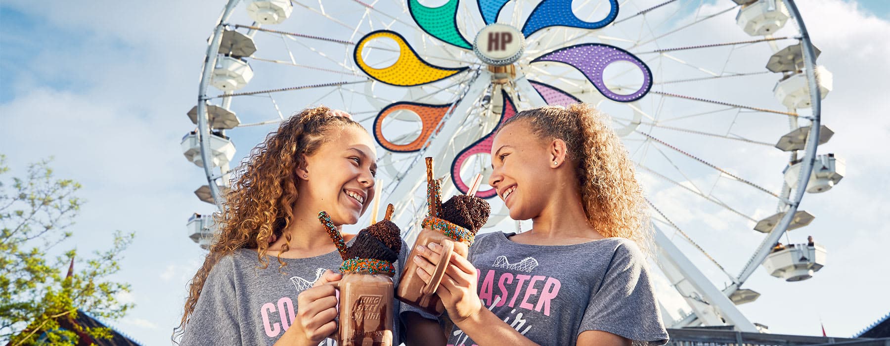 Two little girls with milkshakes standing in front of ferris wheel