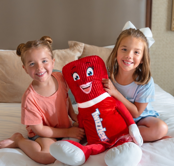 Little girls holding stuffed Twizzler toy on a bed at The Hotel Hershey.